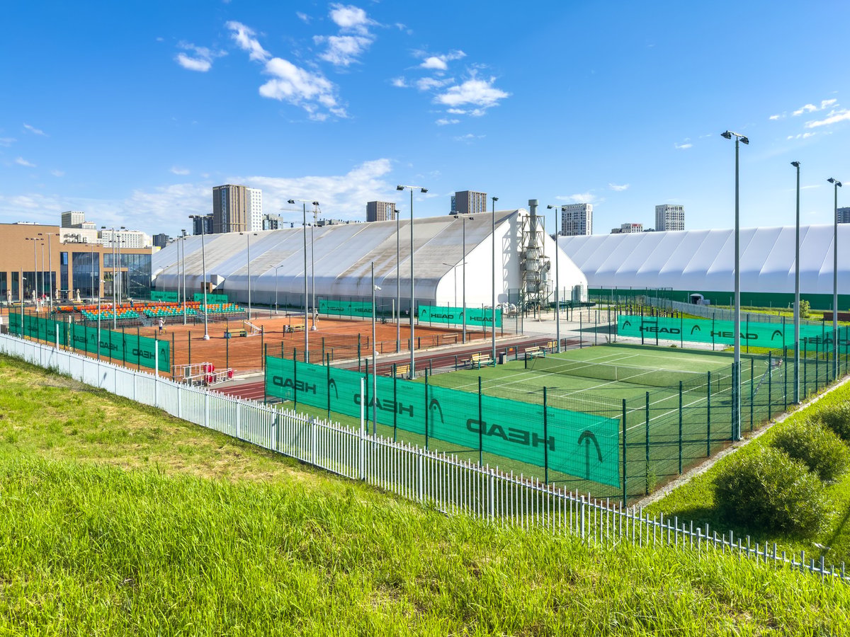 Outdoor tennis courts with green fencing under a clear blue sky
