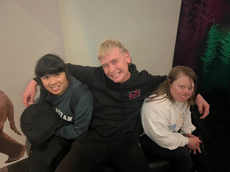 Three young people posing together for a photo indoors, smiling at the camera with arms around each other