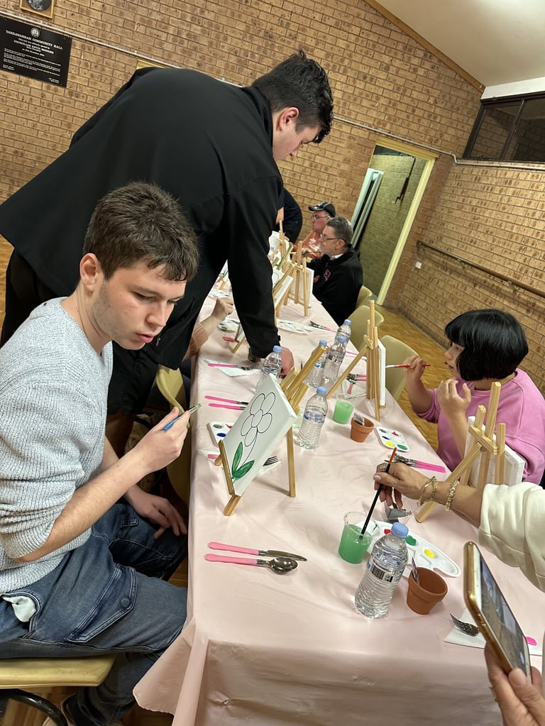 Students painting artwork at easels during an art class activity in a brick-walled indoor space