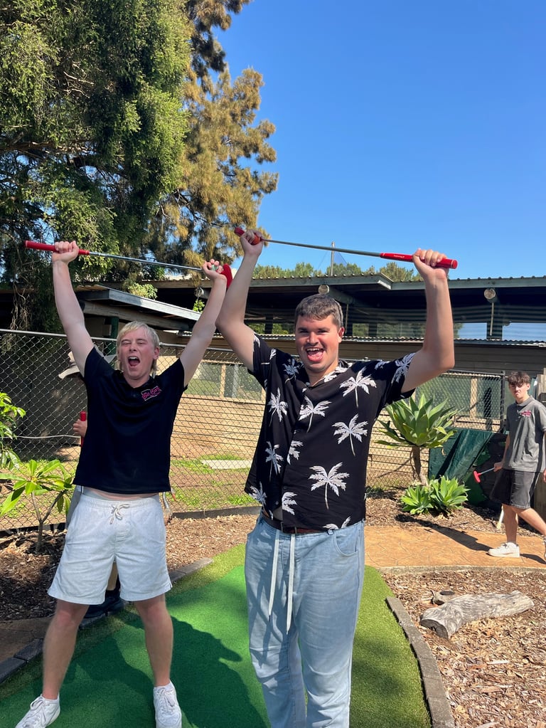Two young men celebrating with putters raised while playing mini golf on a sunny day