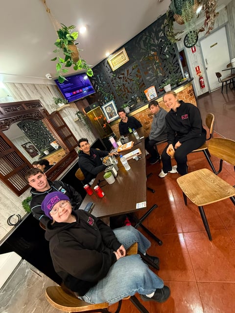Group of four people in black clothing sitting and posing in a modern office space with plants and dark accent wall