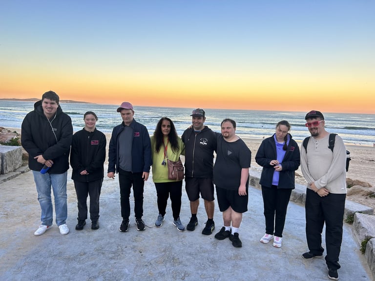 Group of nine people standing together on a beach at sunset with calm ocean and clear sky in the background