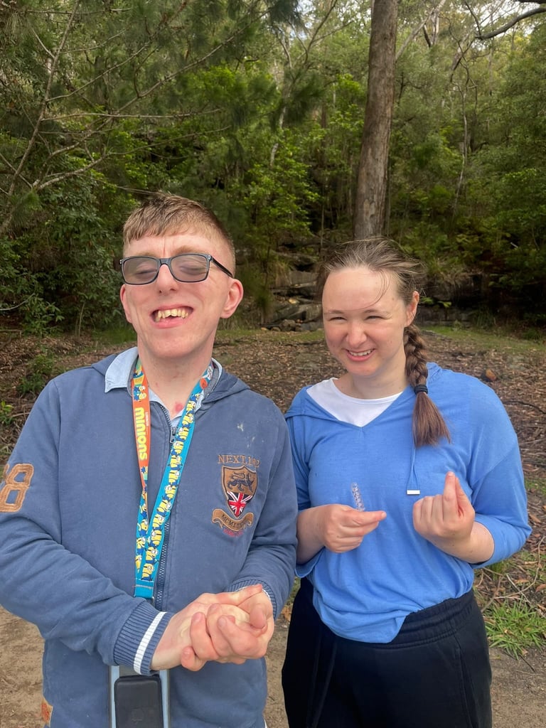 Two young people smiling outdoors wearing casual clothing and lanyards, with forest trees in the background