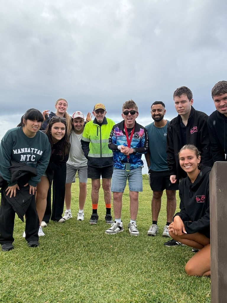 Group of 10 people standing together on a grassy field under a cloudy sky, dressed in casual and athletic wear