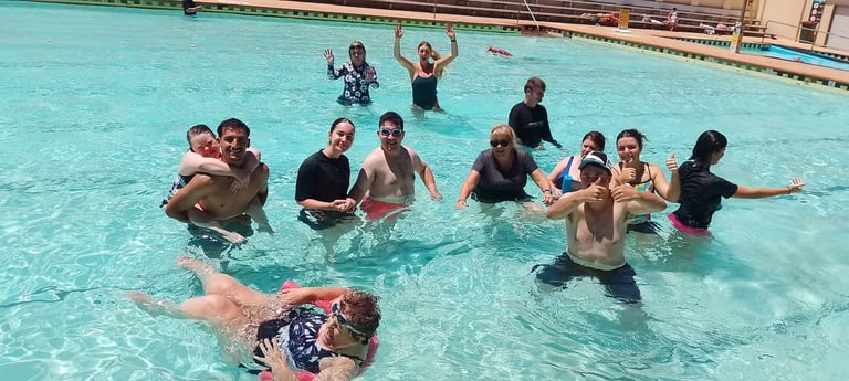 Group of children swimming and playing together in a shallow pool with clear turquoise water on a sunny day