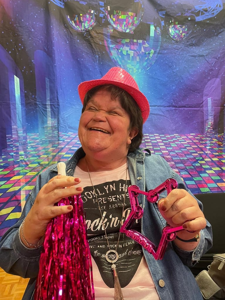 Woman wearing a red cap and denim jacket holding pink sequined fabric in a colorful disco-themed virtual environment