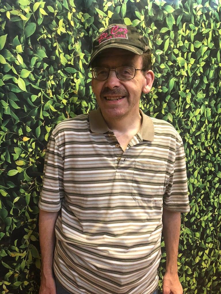 Man wearing striped polo shirt and cap smiling in front of green leaf background