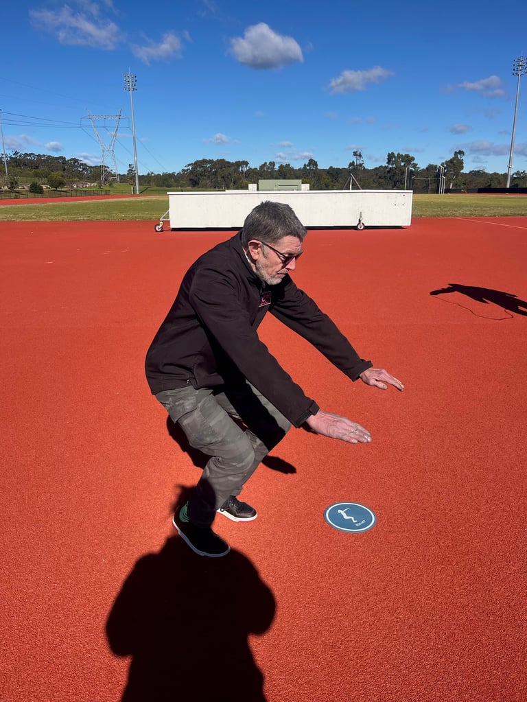 Man in dark blazer bending forward on a red athletic track with a blue circular marker visible on the surface