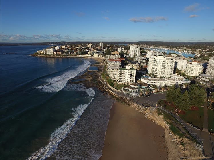 Aerial view of a coastal beach town with high-rise buildings, sandy beaches, and ocean waves, likely an Australian beach city