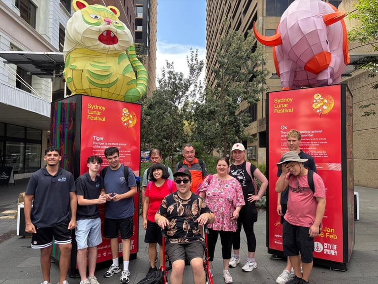 Group of people posing in front of large red banners with yellow cat and pig balloons in an urban street setting