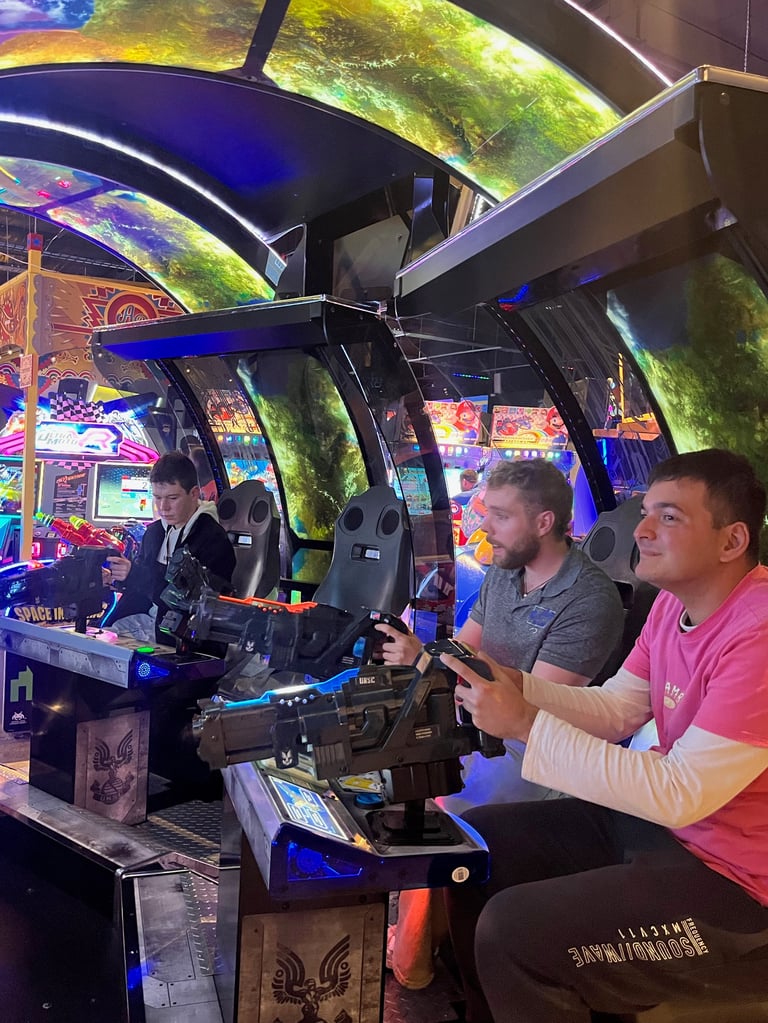 Three men playing video games in an arcade with colorful neon lights and gaming cabinets in the background