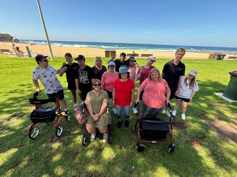 Group of children and adults standing together on a grassy beach field with ocean and blue sky in the background