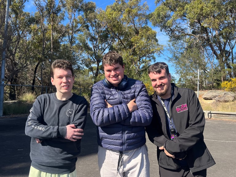 Three young men standing together outdoors on a sunny day with eucalyptus trees in the background
