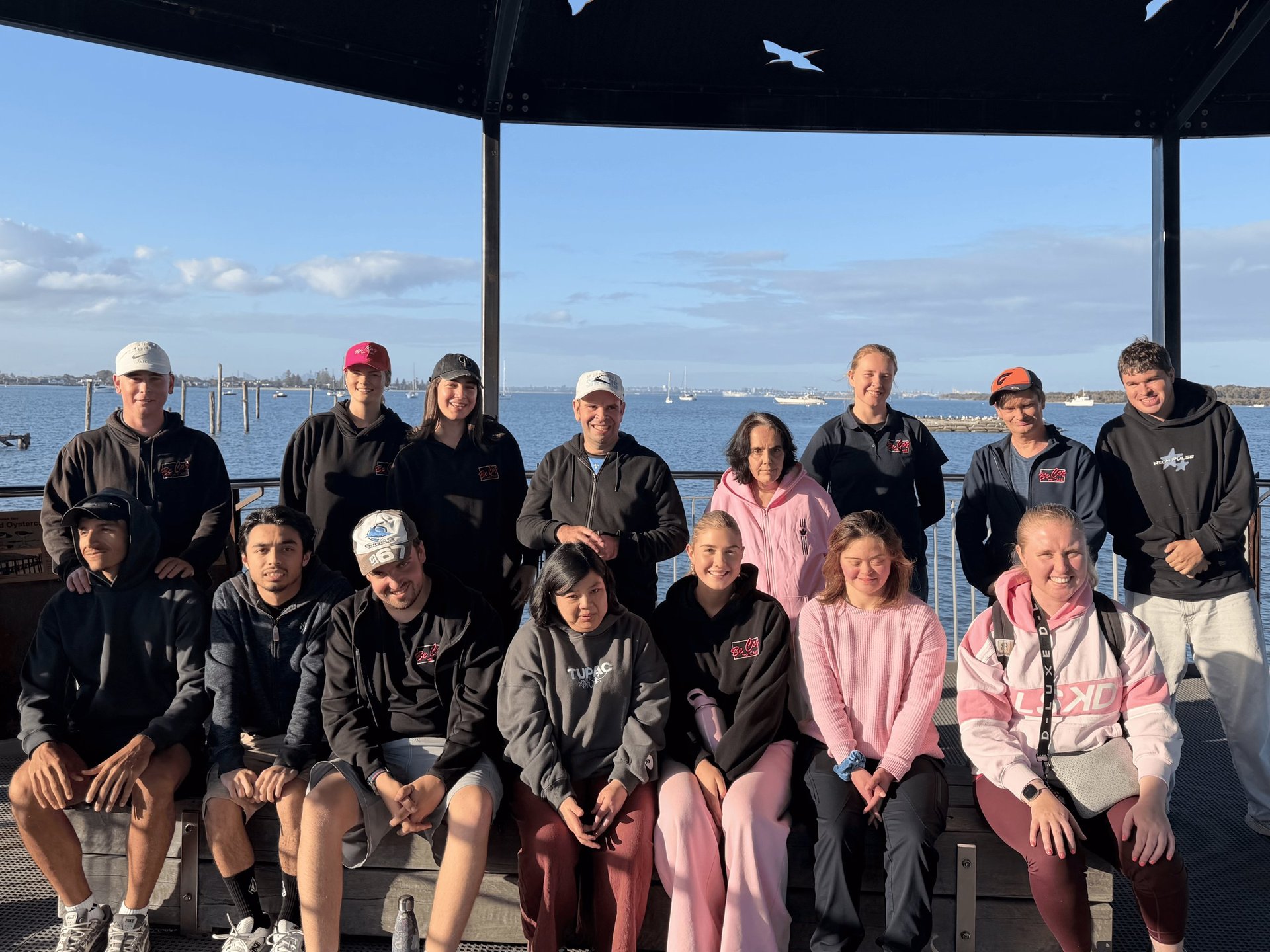 Group of people posing together on a boat deck with water and city skyline in background