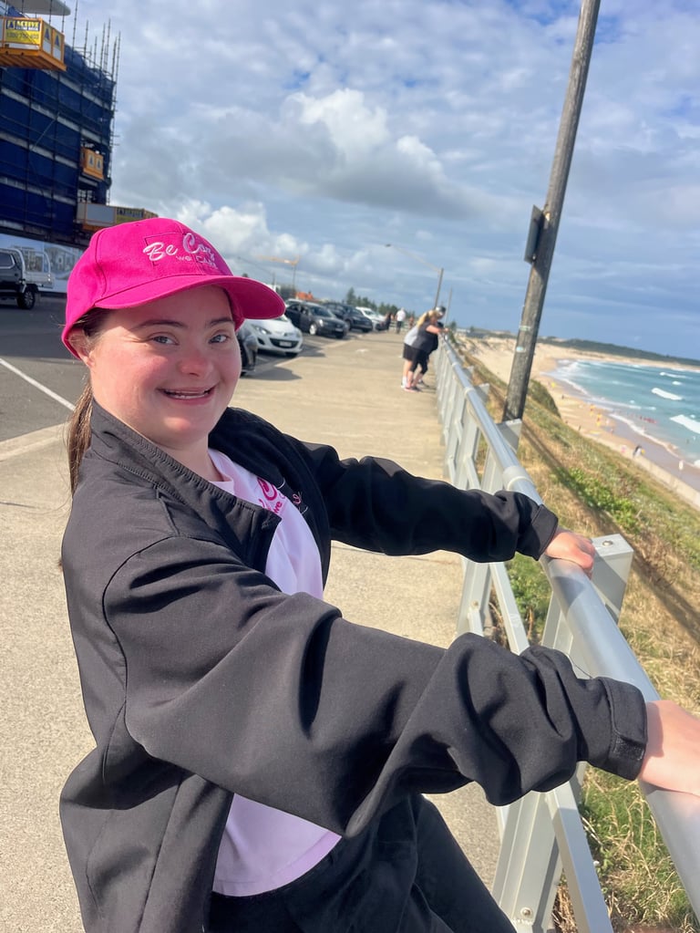 Young girl in pink cap leaning on railing overlooking beach and ocean on sunny day