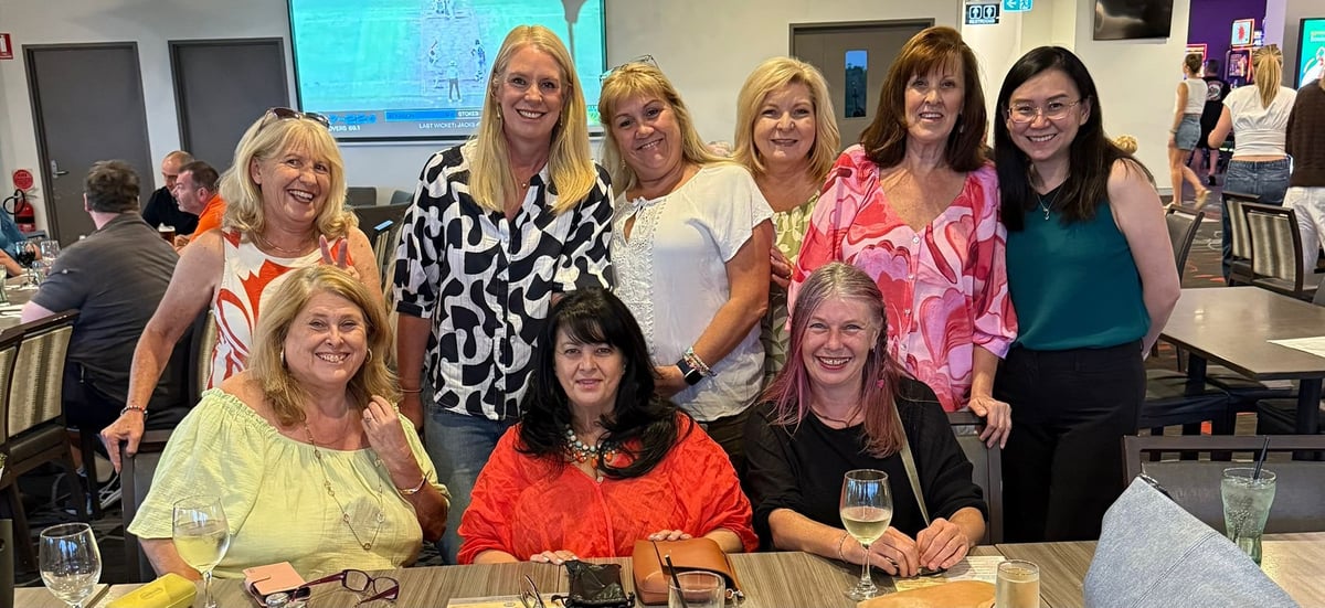 Group of nine women smiling at a table during an indoor gathering or event
