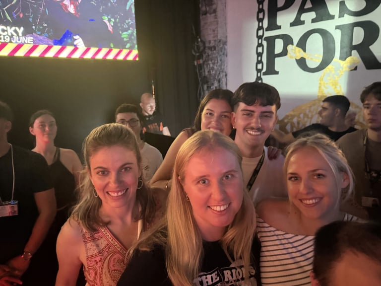 Group of young people smiling at camera at an indoor event with colorful lighting and signage in background