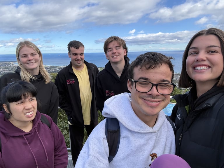 Six smiling teenagers posing together outdoors with ocean and sky in background