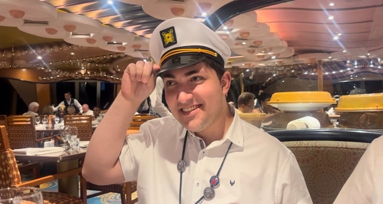 Man in white shirt and captains hat smiling in an upscale dining room on a cruise ship