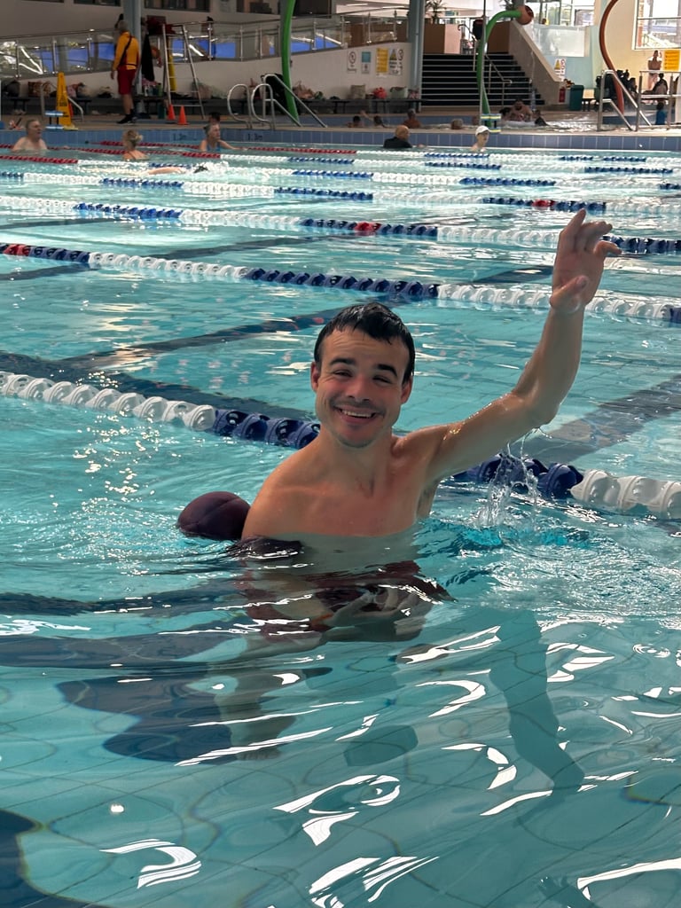 Young swimmer raising his arm in an indoor pool with lane dividers, smiling at the camera