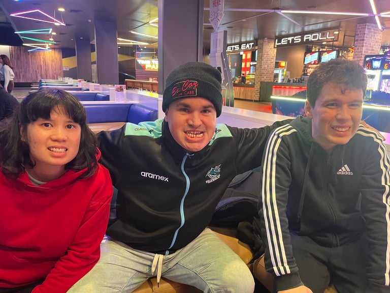 Three smiling teenagers at an indoor arcade or entertainment venue with neon lighting and game machines in the background