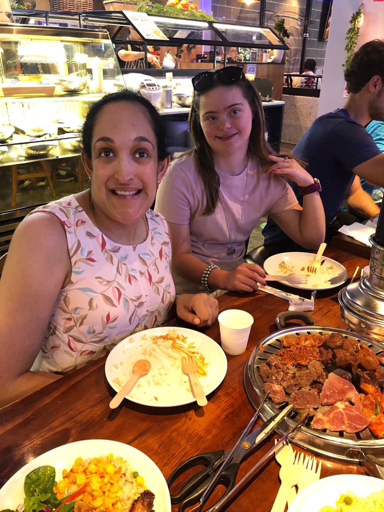 Two smiling young women at a dinner table with food and plates in front of them at a restaurant