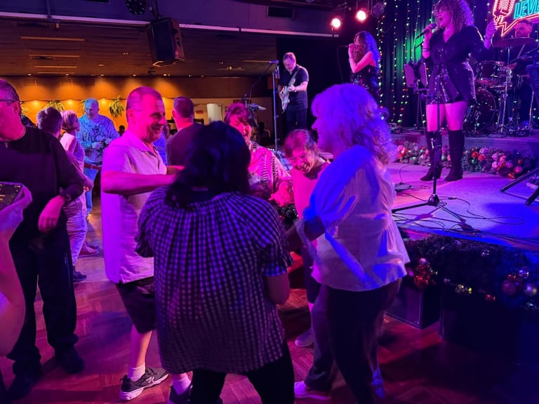 Crowd of people dancing at a concert venue with purple and blue stage lighting and a live band performing