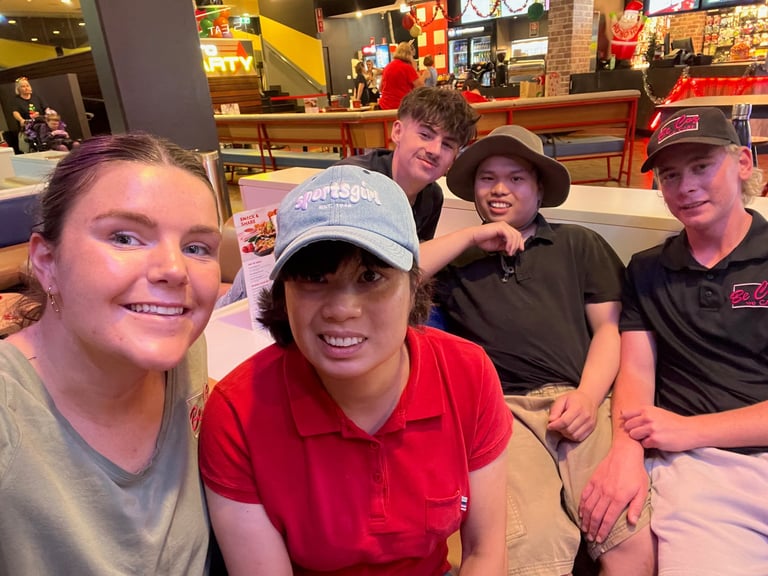 Four smiling young people posing together at an indoor venue with colorful signage and seating in the background