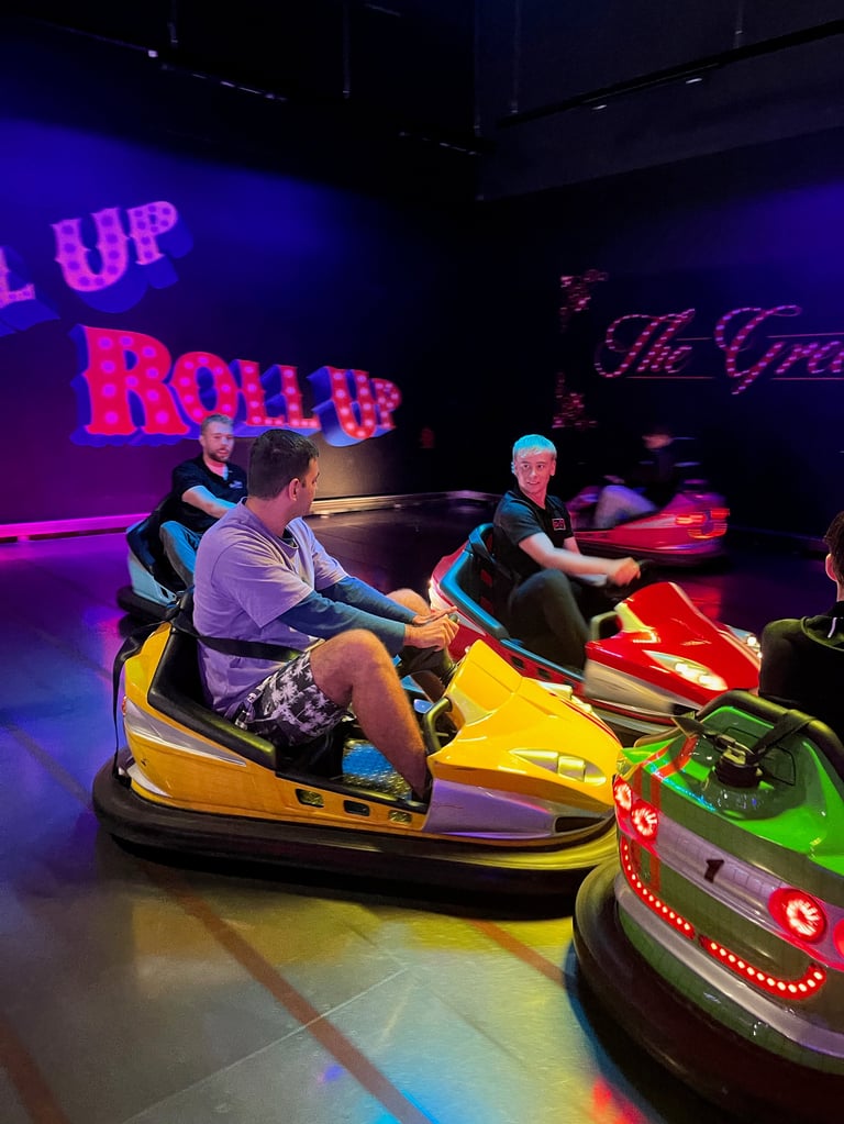 Two people riding in a yellow bumper car at an indoor amusement venue with neon lights and signage in the background