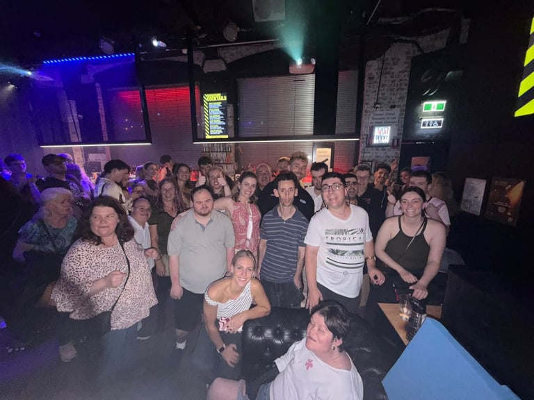Large crowd of people gathered inside a dark nightclub with blue and red lighting, standing and socializing together